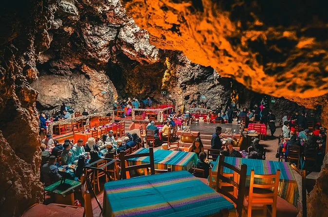 Diners at long tables with striped cloths inside an orange-lit cave
