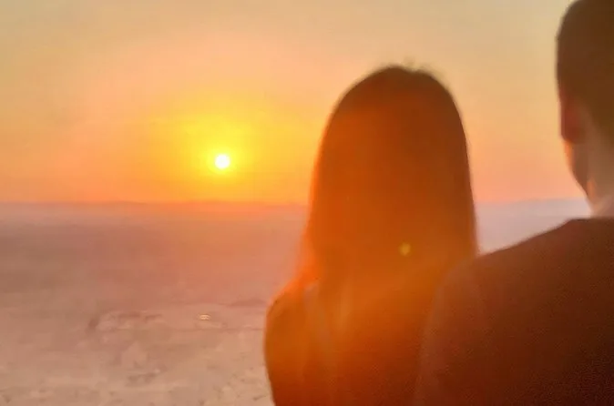 Dos personas vistas de espaldas en la canasta de un globo mirando salir el sol sobre el valle
